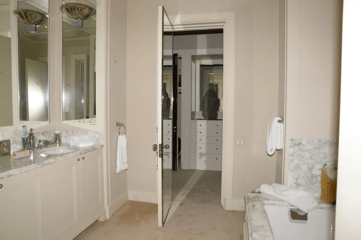 Renovated master bathroom with marble counters, large mirrors and a glass door