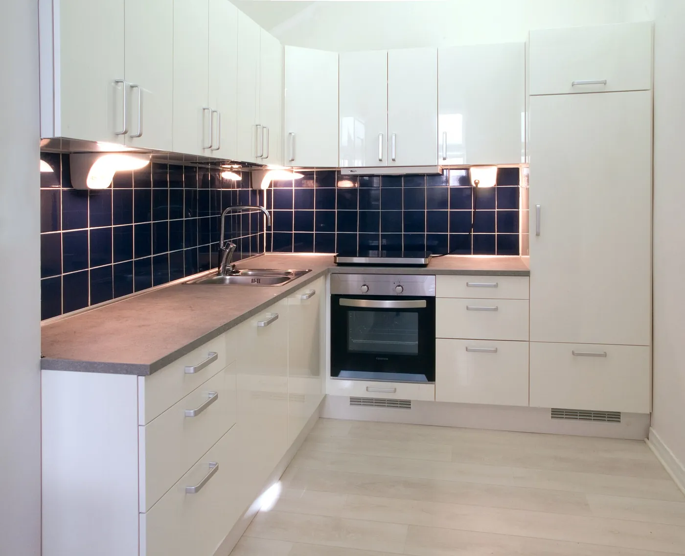 Renovated kitchen with white cabinets, dark blue tiles and integrated oven