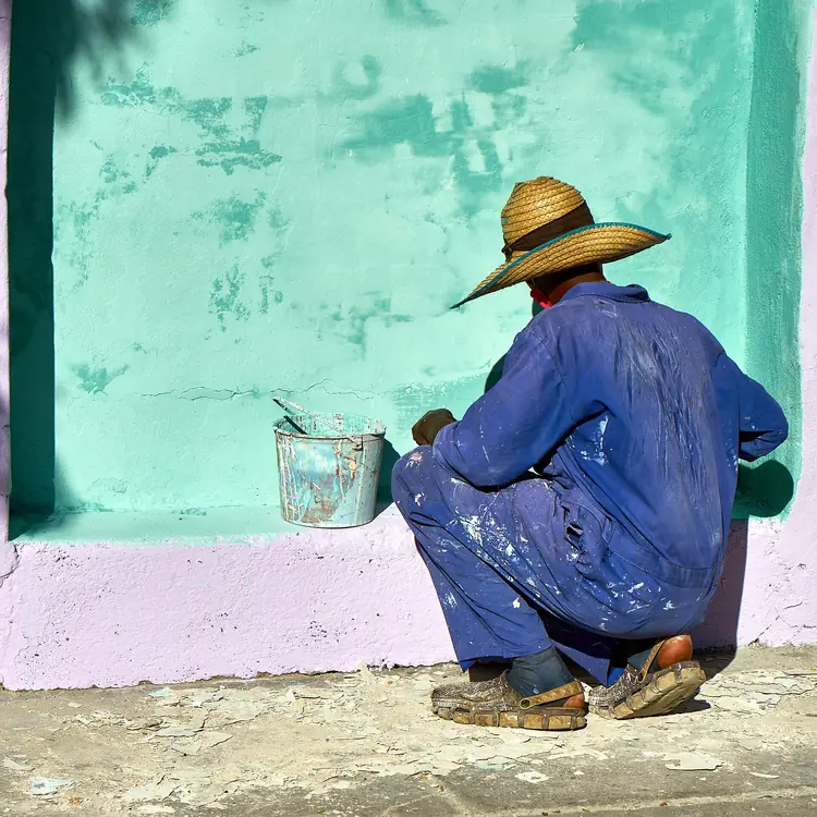 Painter applying paint to an interior wall with a bucket beside him